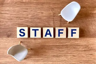 木のテーブルに並んだ「STAFF」の文字の積み木と、向かい合う2脚の小さな椅子
