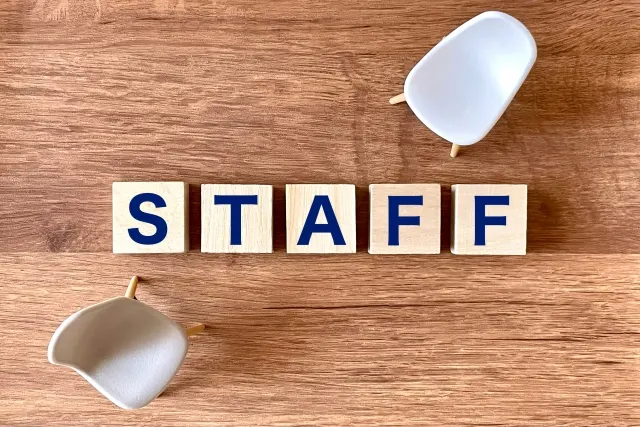 木のテーブルに並んだ「STAFF」の文字の積み木と、向かい合う2脚の小さな椅子